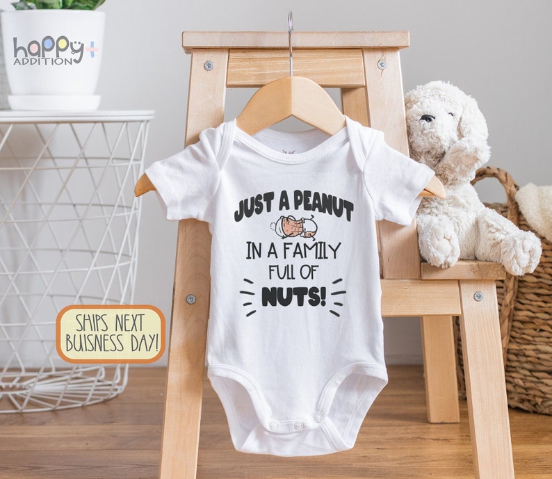 May include: White baby onesie with a peanut graphic and the text "Just a peanut in a family full of nuts!"
