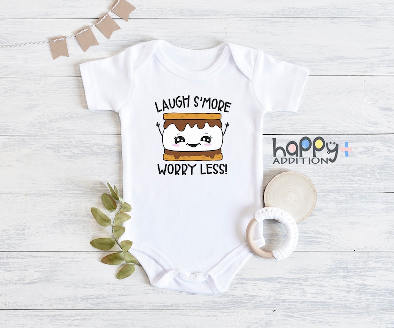 Pu&ograve; includere: Body bianco per neonato con un grafico di marshmallow arrostito e il testo "Laugh S'more Worry Less!"