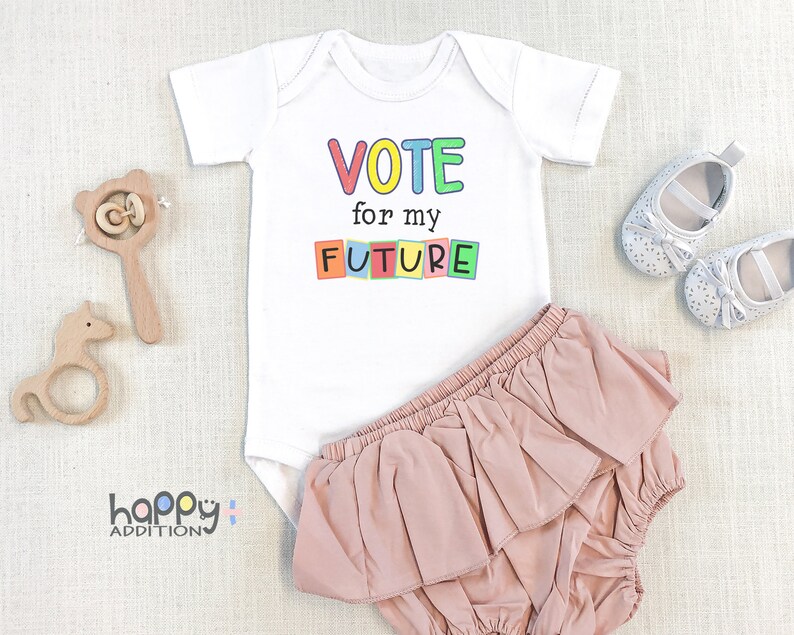 May include: White baby onesie with the text "VOTE for my FUTURE" in colorful block letters. The onesie is paired with a pink ruffled diaper cover.