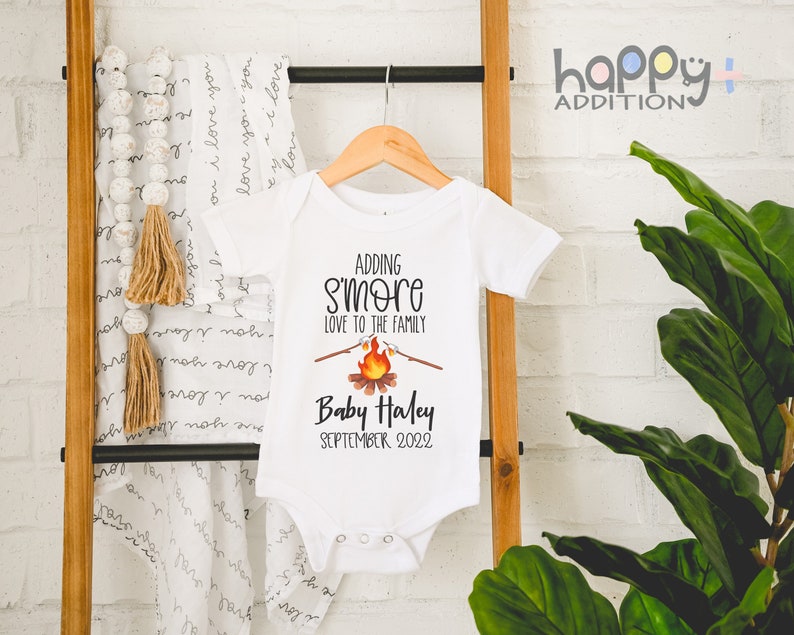 May include: White onesie with a campfire graphic and the text "Adding S'more Love to the Family" and "Baby Haley September 2022".