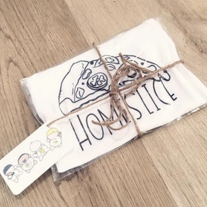 May include: A white t-shirt with a black and white illustration of a pizza slice and the text "Home Slice". The t-shirt is wrapped in brown paper and tied with twine. A small tag with a cartoon illustration of four people is attached to the package.