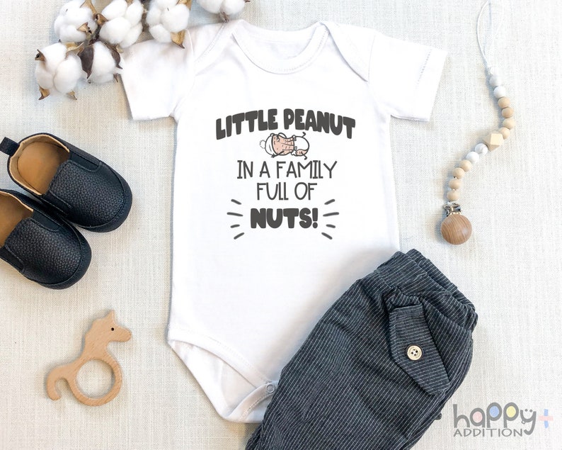 May include: White baby onesie with the text "Little Peanut in a family full of nuts!" and a cartoon peanut in a onesie. The onesie is paired with gray striped pants.
