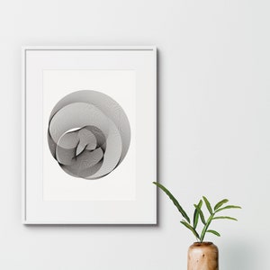 Op de afbeelding: Een zwart-witte abstracte geometrische print in een wit frame aan een witte muur met een groene plant in een houten vaas.