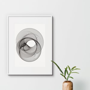 Può includere: Una stampa di arte astratta in bianco e nero in una cornice bianca, appesa a un muro bianco. Una piccola pianta in vaso con foglie verdi è in primo piano.