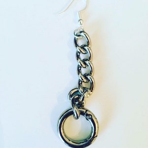 May include: A single silver-toned earring featuring a chain design and a large circular clasp. The earring has a hook for pierced ears. The chain links are thick and chunky, giving the earring a bold, modern look. The earring is set against a white background.