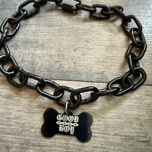 May include: Black chain dog collar with a bone-shaped tag. The tag has the words "GOOD BOY" in white lettering. The collar is made of large, glossy black links.