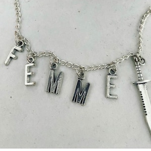 May include: A silver chain necklace with the word "FEMME" spelled out in charms, and a small silver knife charm.