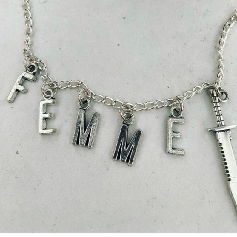May include: A silver chain necklace with the word "FEMME" spelled out in charms, and a small silver knife charm.