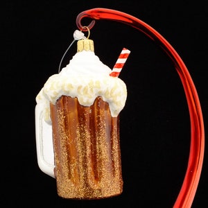 May include: A glass ornament shaped like a root beer float with a red and white striped straw. The ornament is decorated with white frosting and brown root beer.
