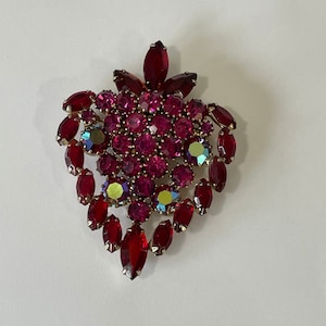 May include: A vintage brooch in a floral design, featuring a cluster of red and fuchsia-colored rhinestones. The brooch has a gold-tone metal setting and iridescent accents, creating a sparkling effect. The brooch is a statement piece.