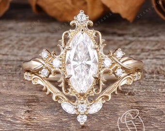 May include: A gold-colored engagement ring set with a marquise-cut diamond and smaller accent diamonds. The ring features an ornate, vintage-inspired design with intricate filigree details. The band is also adorned with small diamonds.