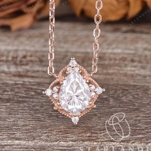 May include: A pear-shaped diamond pendant necklace with a rose gold chain and a delicate halo setting. The pendant features a pear-shaped diamond surrounded by smaller diamonds.