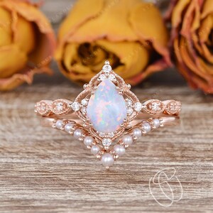 May include: A pear-shaped opal engagement ring set in rose gold with a delicate pearl and diamond band. The ring features a vintage-inspired design with intricate details.
