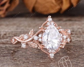 Puede incluir: Un anillo de compromiso de diamante de forma pera engastado en oro rosa con un delicado diseño floral. El anillo presenta una piedra central de forma pera rodeada de diamantes más pequeños y detalles intrincados de hojas.