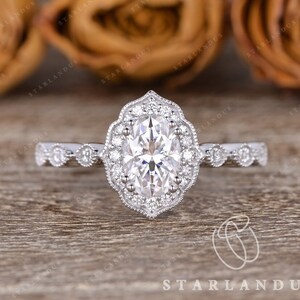 May include: A silver engagement ring with a large oval-shaped center stone surrounded by smaller diamonds. The ring has a delicate, vintage-inspired design with a halo setting and a milgrain band.