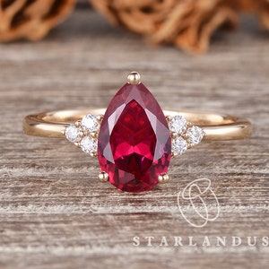 May include: A pear-shaped ruby engagement ring set in gold with a halo of smaller diamonds.