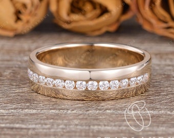 May include: A gold wedding band with a row of small diamonds set in a channel setting. The band is on a wooden surface.