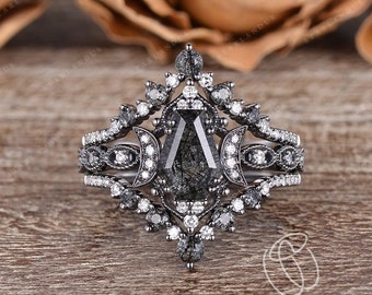 May include: A black pear-shaped engagement ring with a black diamond center stone and a halo of smaller diamonds. The ring is set in a black metal band and features a delicate moon design on either side of the center stone.