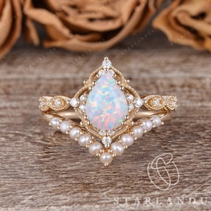 May include: A pear-shaped opal engagement ring set in gold with a delicate pearl band. The ring features a vintage-inspired design with intricate details and sparkling diamonds.