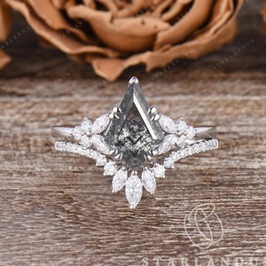 May include: A pear-shaped black diamond engagement ring with a delicate, floral-inspired band. The ring is set in white gold and features a halo of smaller diamonds.