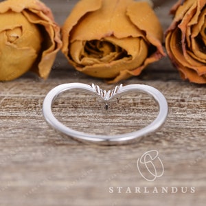 May include: A silver ring with a heart-shaped design and three small diamonds. The ring is on a wooden surface with dried flowers.