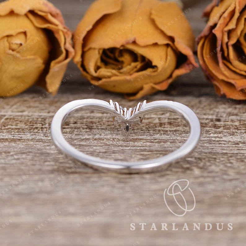 May include: A silver ring with a heart-shaped design and three small diamonds. The ring is on a wooden surface with dried flowers.