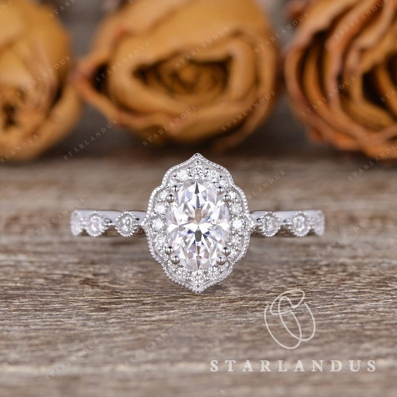 May include: A silver engagement ring with a large oval-shaped center stone surrounded by smaller diamonds. The ring has a delicate, vintage-inspired design with a halo setting and a milgrain band.