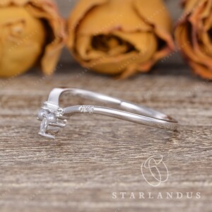 May include: A delicate silver ring with a curved band and a small cluster of diamonds and pearls. The ring is set against a backdrop of brown wood and yellow roses.