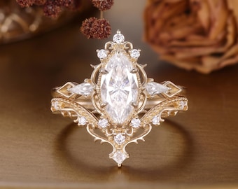 Può includere: Un set di anelli in oro con una pietra centrale taglio marquise circondata da pietre più piccole rotonde e a goccia. La fascia e la montatura presentano una lavorazione del metallo complessa con dettagli appuntiti e motivi in filigrana.