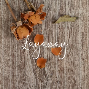 Puede incluir: Pétalos y capullos de rosa secos sobre un fondo de madera con la palabra "Layaway" escrita en cursiva blanca.