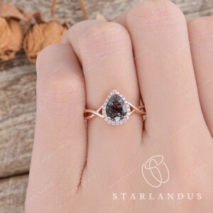 May include: A rose gold engagement ring with a pear-shaped black diamond center stone and a halo of smaller diamonds. The band is twisted and features a delicate design.
