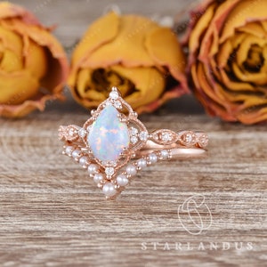 May include: A pear-shaped opal engagement ring set in rose gold with a delicate diamond and pearl band. The ring features a vintage-inspired design with intricate details.