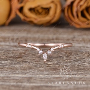 May include: A delicate rose gold wedding band with a curved design. The band is adorned with small diamonds and pearls.