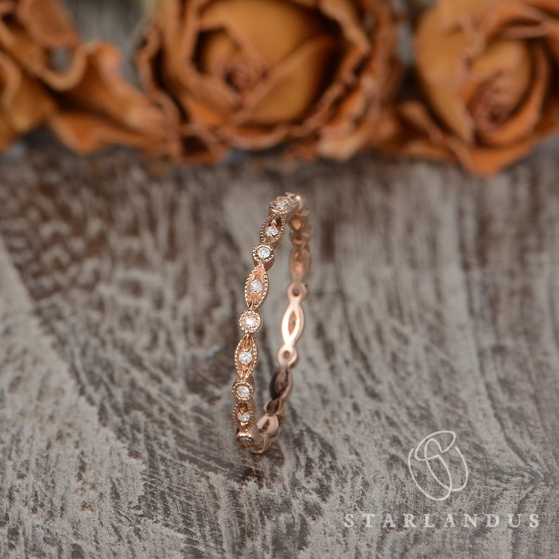Op de afbeelding: Een delicate ros&eacute;gouden band met een rij kleine, ronde diamanten die zijn gezet in een delicaat, ovaalvormig ontwerp.