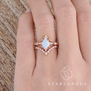 May include: A pear-shaped opal engagement ring set in rose gold with a delicate floral design and a matching band with small pearls. The ring is on a finger.
