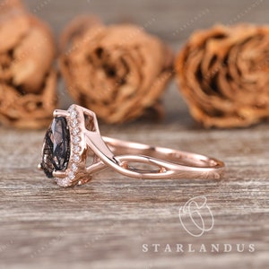 May include: A rose gold engagement ring with a pear-shaped smoky quartz gemstone surrounded by a halo of smaller diamonds. The ring band is a delicate twisted design.