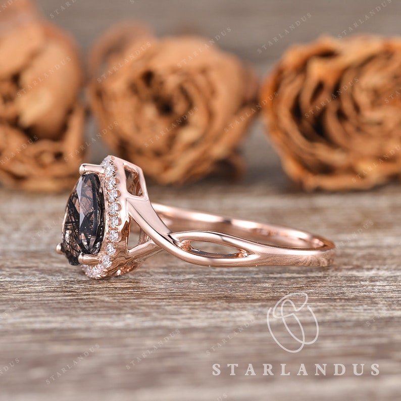 May include: A rose gold engagement ring with a pear-shaped smoky quartz gemstone surrounded by a halo of smaller diamonds. The ring band is a delicate twisted design.