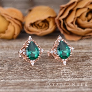 May include: A pair of rose gold earrings with pear-shaped emerald green gemstones surrounded by a halo of smaller white gemstones.
