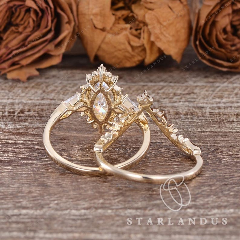 Puede incluir: Un conjunto de anillos de oro que incluye un anillo de compromiso con una piedra central de corte marquesa rodeada por un halo de piedras peque&ntilde;as, junto a una alianza curva adornada con una hilera de piedras peque&ntilde;as en oro pulido.