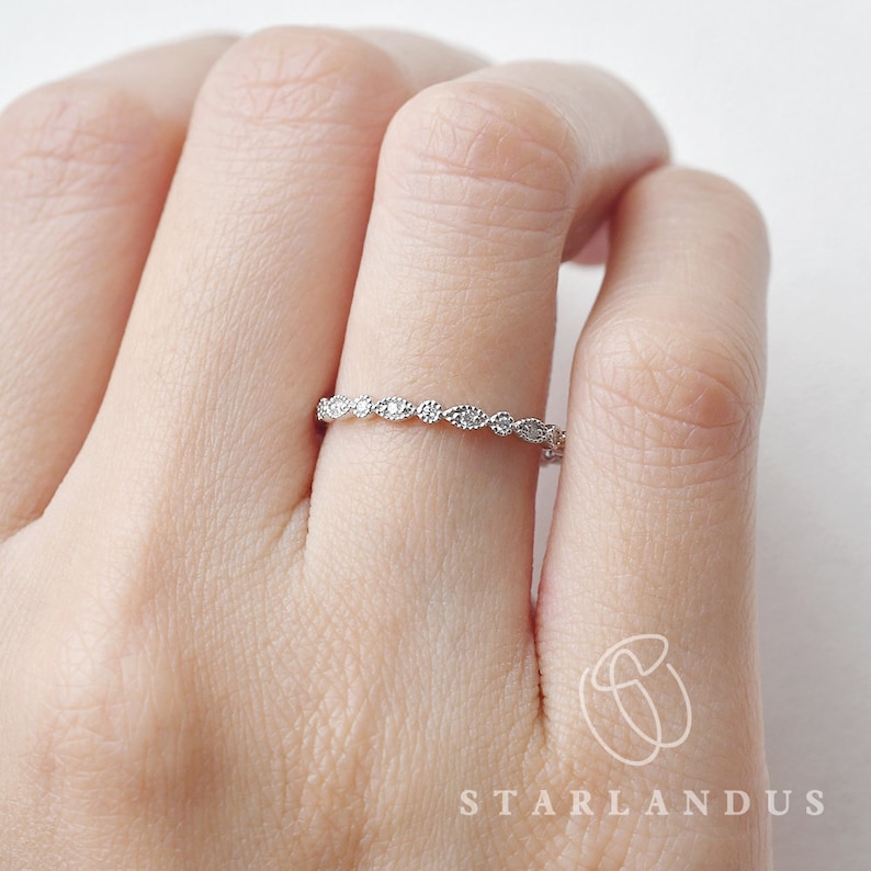 Op de afbeelding: Een delicate zilveren ring met een rij kleine, heldere, ronde stenen in een gegolfd ontwerp.