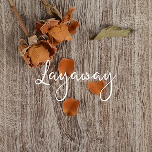 May include: Dried rose petals and buds on a wooden background with the word "Layaway" written in white cursive.