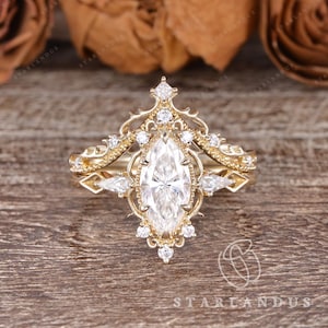 Puede incluir: Un anillo de oro con una piedra central de corte marquesa rodeada por un marco de filigrana decorativo. La banda y el engaste est&aacute;n acentuados con m&uacute;ltiples piedras peque&ntilde;as redondas y de corte pera dispuestas en un patr&oacute;n sim&eacute;trico.