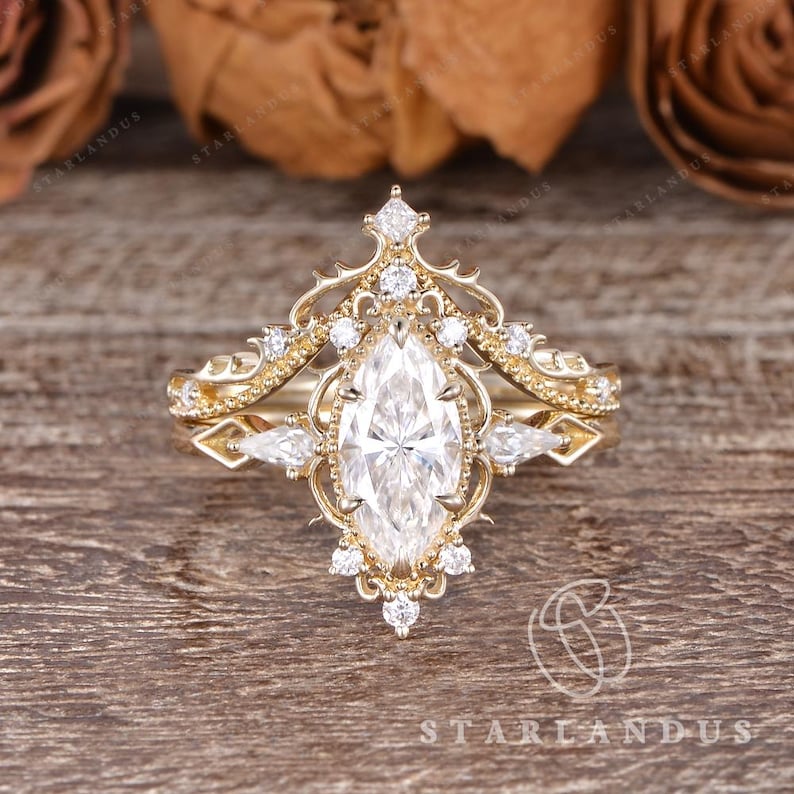 Puede incluir: Un anillo de oro con una piedra central de corte marquesa rodeada por un marco de filigrana decorativo. La banda y el engaste est&aacute;n acentuados con m&uacute;ltiples piedras peque&ntilde;as redondas y de corte pera dispuestas en un patr&oacute;n sim&eacute;trico.