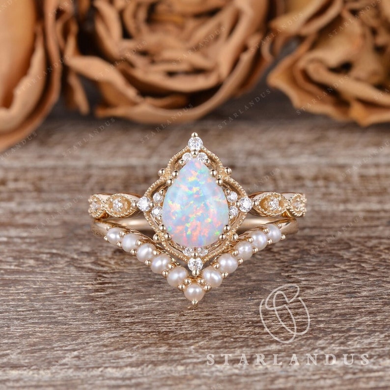 May include: A pear-shaped opal engagement ring set in gold with a delicate pearl band. The ring features a vintage-inspired design with intricate details and sparkling diamonds.