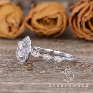 May include: A silver engagement ring with a large oval-shaped center stone surrounded by smaller stones. The band is adorned with a delicate design of smaller stones.