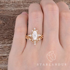 Puede incluir: Un conjunto de anillos de oro con una piedra central de corte marquesa rodeada de piedras m&aacute;s peque&ntilde;as redondas y de corte marquesa en una banda decorativa de filigrana. El dise&ntilde;o incluye metalurgia intrincada y una banda en forma de V.