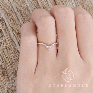 May include: A delicate silver ring with a V-shaped design and small sparkling stones. The ring is worn on a finger.