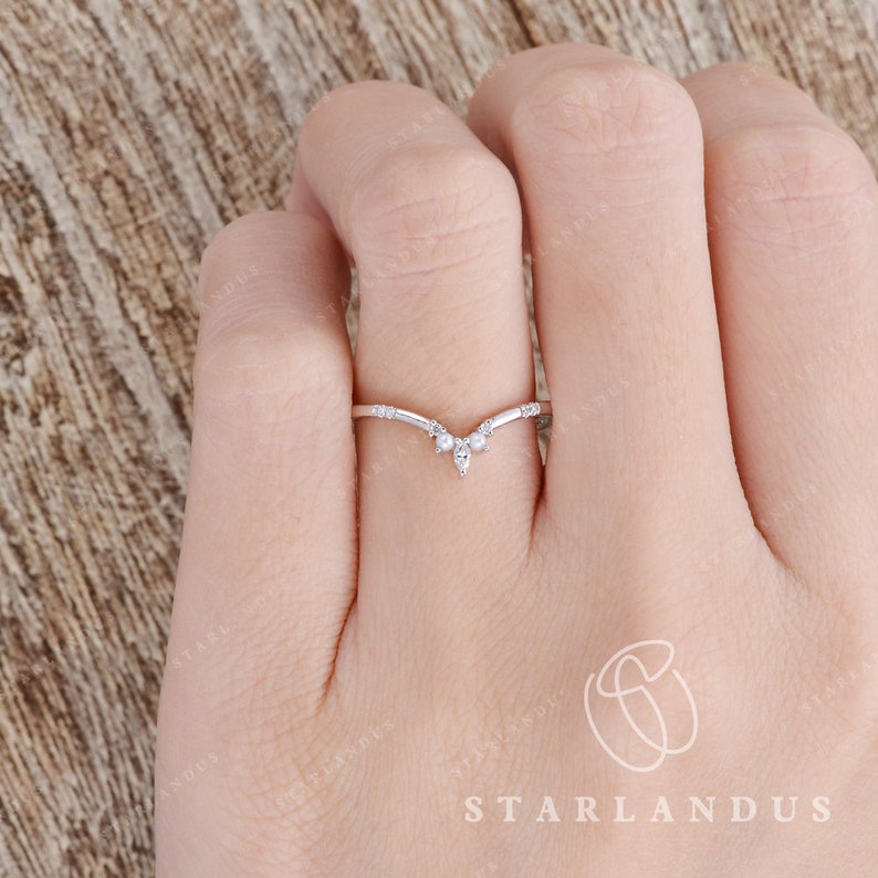 May include: A delicate silver ring with a V-shaped design and small sparkling stones. The ring is worn on a finger.