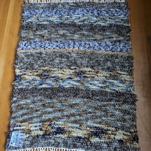 May include: A woven rug with a fringe border in shades of brown, blue, and white. The rug has a textured, hand-woven look.