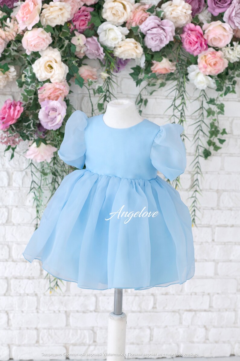 May include: A light blue tulle dress with puffed sleeves and a round neckline. The dress is on a white mannequin and has the word "Angelove" printed on the skirt.
